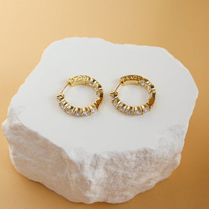 Thea gold CZ eternity hoop earrings, 20mm across, displayed on a white stone