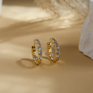 Pair of Thea gold hoop earrings with nine round CZ stones set front and back, on a soft beige background