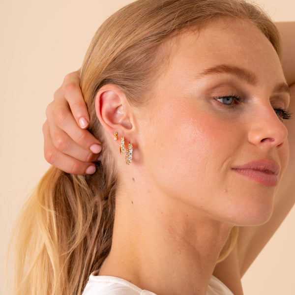 Side profile of a model wearing Thea gold eternity hoop earrings in a three-piece ear stack