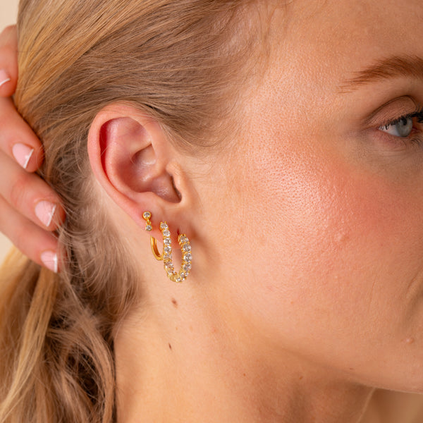Close-up of the Thea 20mm CZ eternity hoop worn in the lobe with gold huggie hoops and a double-drop stud