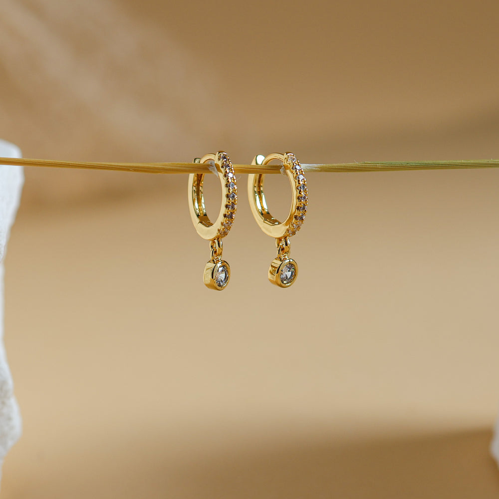 Rhea pavé huggie drop earrings in 18K gold plate, small CZ-set hoops with a round cubic zirconia drop, hanging on a gold wire