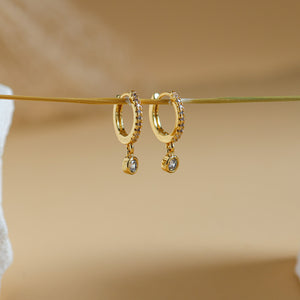 Rhea pavé huggie drop earrings in 18K gold plate, small CZ-set hoops with a round cubic zirconia drop, hanging on a gold wire
