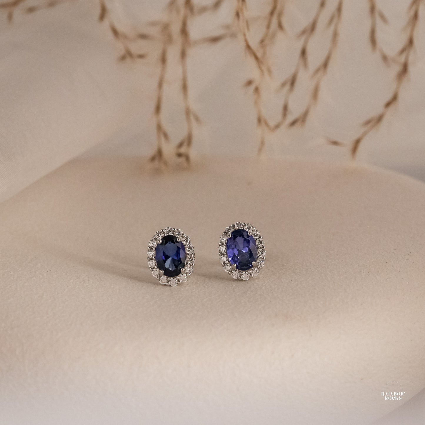 Pair of sapphire earrings with diamond accents on a beige surface.